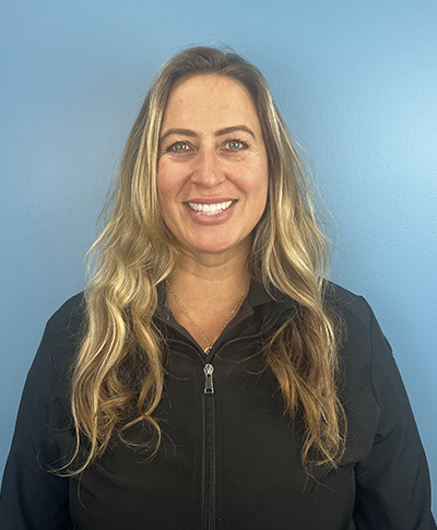 The image shows a woman posing with a blue background behind her. She has long hair and is wearing casual attire, including a jacket.