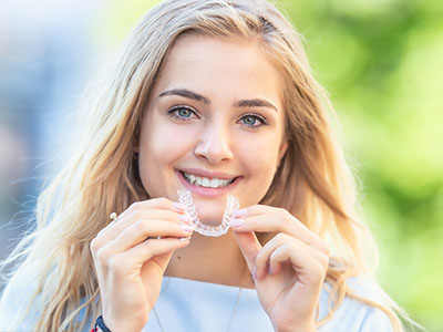 The image features a young female with blue eyes smiling at the camera while holding a toothbrush in her hand.