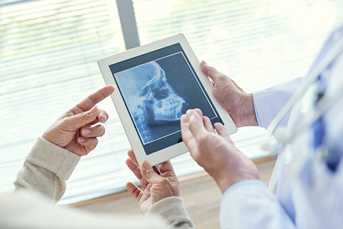 The image features two individuals, one holding a tablet displaying an X-ray, being shown the image by a healthcare professional who appears to be a radiologist or medical expert.